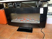 Front view of Well Universal Ember Hearth electric fireplace with orange glowing ember effect, on black stand with power cord visible. Shows fireplace powered on with flame effect.
