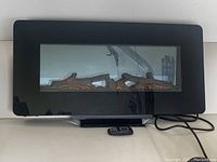 Front view of the electric fireplace showing the black curved glass front, realistic log display inside, power cord, and remote control on a white couch.