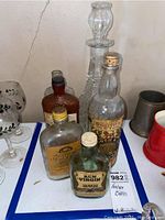 Overall view of the lot showing five antique/vintage spirit bottles and a glass decanter with stopper on table surface.