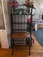 Front view of the black metal frame bakers rack with wooden shelves and decorative scroll design