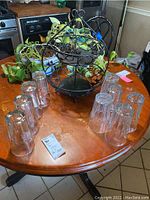 Photo of nine clear commercial bar glasses arranged upside down around a two-tier metal fruit basket on a wooden table.