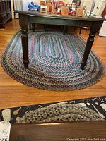 Oval braided multicolored area rug under a wooden table on hardwood floor.
