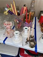 Wide view showing various glass candle holders, candles, and decorative vase on a table with other glassware and bottles in background.