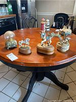 Photo of a round wooden table displaying multiple carousel horse music boxes and a snowglobe with a crystal-like sphere on a floral base.