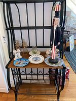View of all items arranged on a wooden shelf with a black metal frame including a tall wooden Uncle Sam figure and various plates, angel figurines, and candle holders