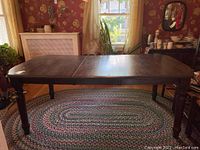 Wooden dining table with visible scratches, stains, marks on the surface, and four turned legs, shown from side angle showing the table length and damaged areas.