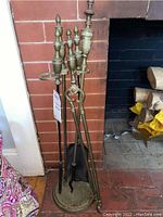Full view of the fireplace accessory set including four brass and black metal pokers, black metal dustpan, tongs, and hammered brass stand.