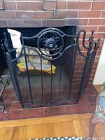 Full view of black metal fireplace screen with mesh panels and circular floral centerpiece, positioned in front of a brick fireplace