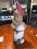 Front view of the ceramic garden gnome detailing the face, red pointed hat, apron, and pipe.