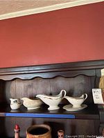 Five ceramic gravy boats and creamers displayed on a wooden shelf, showing size and style variety