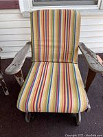Front view of outdoor rocking chair with striped yellow, red, blue, and green cushion on seat and backrest. Armrests show paint chipping.