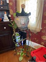 Potted pothos plant in ceramic pot on metal stand near window.