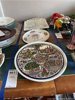Photo shows five decorative platters laid out on a table with other items in the background. Included is the detailed colorful Holy Land memorial platter, floral patterned platter, clear glass scalloped platter, and other decorative platters.