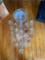 Photo showing the large punch bowl with 20 matching etched crystal leaf punch cups arranged on wooden floor.