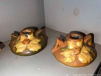 Photo of one Roseville Pottery candle holder with floral design and two handles, shown from a side angle to highlight shape and glaze.