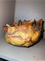 Side view of Roseville hanging planter displaying yellow and brown raised floral design and rope handles.