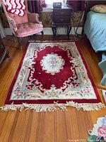 Full view of the six foot rectangular area rug lying on a wooden floor, showing the dominant red color and central floral design