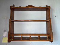 Full view of wooden wall shelf showing three shelves, side supports, and spindle rail on bottom shelf.