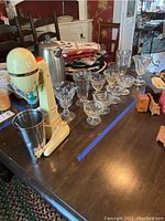 Full view of soda fountain machine alongside 10 glassware pieces on wooden table, showing condition and variety of glasses.