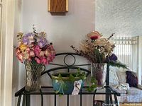 Full view of two glass vases with faux flowers and ceramic potted plant on display table