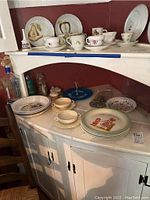 Overview of vintage dinnerware and glass decor on white shelf with maroon wall background.
