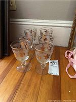 Set of six stemware glasses arranged on wooden floor, showing frosted and gold leaf detail