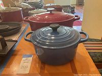 Wide view showing both red Cuisinart and blue Le Creuset enameled cast iron Dutch ovens on wooden table