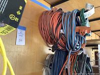 Multiple outdoor extension cords coiled and stacked showing colors and length.
