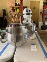 KitchenAid stand mixer white with two large mixing bowls, one in use on mixer, one in foreground, showing handles and reflective stainless steel finish