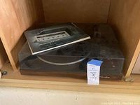 Turntable inside wooden cabinet with dust cover closed and instruction manual on top