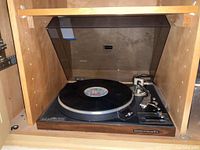 Record player installed in wooden cabinet, dust cover open, vinyl on platter
