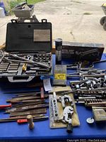 Full lot view showing socket sets, grease gun, hand tools laid out on blue surface outside garage