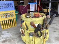 Yellow fabric tool bucket filled with a variety of hand tools visible inside the bucket and in outer pockets on the sides.