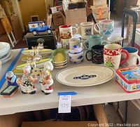Wide view of the collection showing variety of mugs, figurines, salt and pepper shakers, and collectible tins on a table.