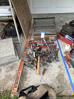 Overview of wrenches, sockets, socket tray, mallet, long orange level on concrete ground with assorted tools and parts around