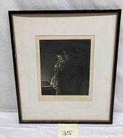 Framed etching artwork showing a woman holding a child, placed against a white background with a visible lot number tab.