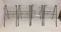 Four clear acrylic folding chairs lined up side by side