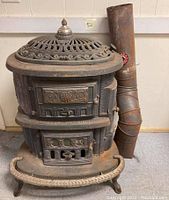 Front view of antique cast iron wood burning stove with ornate vented top, firebox door, and flue pipe