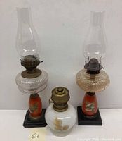 Full view of three antique oil hurricane lamps showing two tall lamps with chimneys and a shorter one without chimney