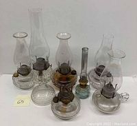 All seven oil hurricane lamps arranged in a group showing their varying base shapes and chimneys.