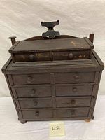 Front view of antique wooden gentleman's chest with eight drawers and two small drawers on top, showing signs of wear and one leg replaced.
