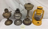 Four kerosene lamps of varying styles on white cloth background, showing all items in the lot