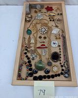 Full view of costume jewelry collection laid out on a wooden tray including necklaces, bracelets, earrings, brooches, and wrist timer.