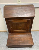 Front view of the closed wooden slant front cabinet showing the slanted lid and the door below.
