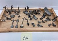 Full set of pewter miniatures displayed on a wooden tray, showing multiple animals, sleds, spoons, and figures arranged closely together.