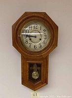 Full view of the clock hanging on the wall showing wooden octagonal frame and pendulum compartment below.