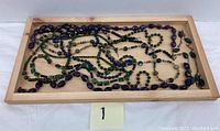 Photo showing all gemstone jewelry strands laid out on a wooden tray, illustrating variety and colors of amethyst, jade, onyx, lapis, and glass beads.