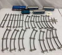 Full set of vintage tin train cars and multiple track pieces laid out on a white surface.
