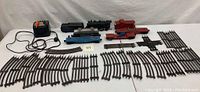 Wide shot showing Lionel transformer, steam engine, three freight cars, and various track pieces laid out on white backdrop.