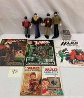 Four Beatles figurines, Batman trading cards, five comic books from various series including Raiders of the Lost Ark, X-Men, Hard Boiled, and Mad magazines.